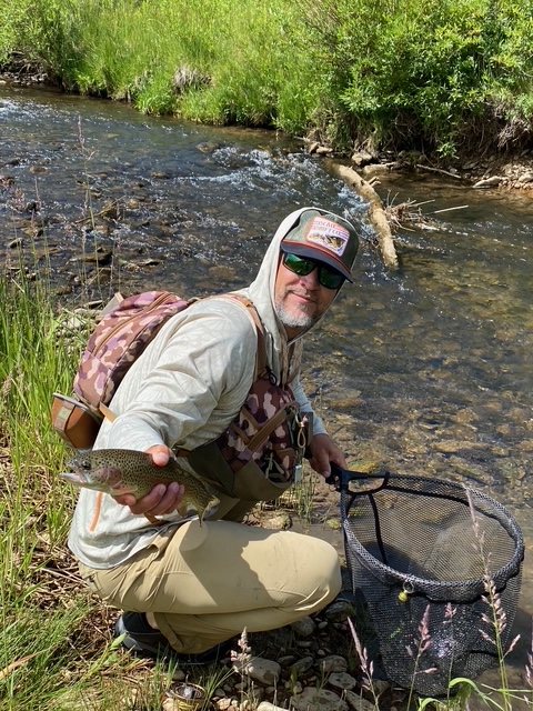 Walk and wade angler holding a trout beside a stream